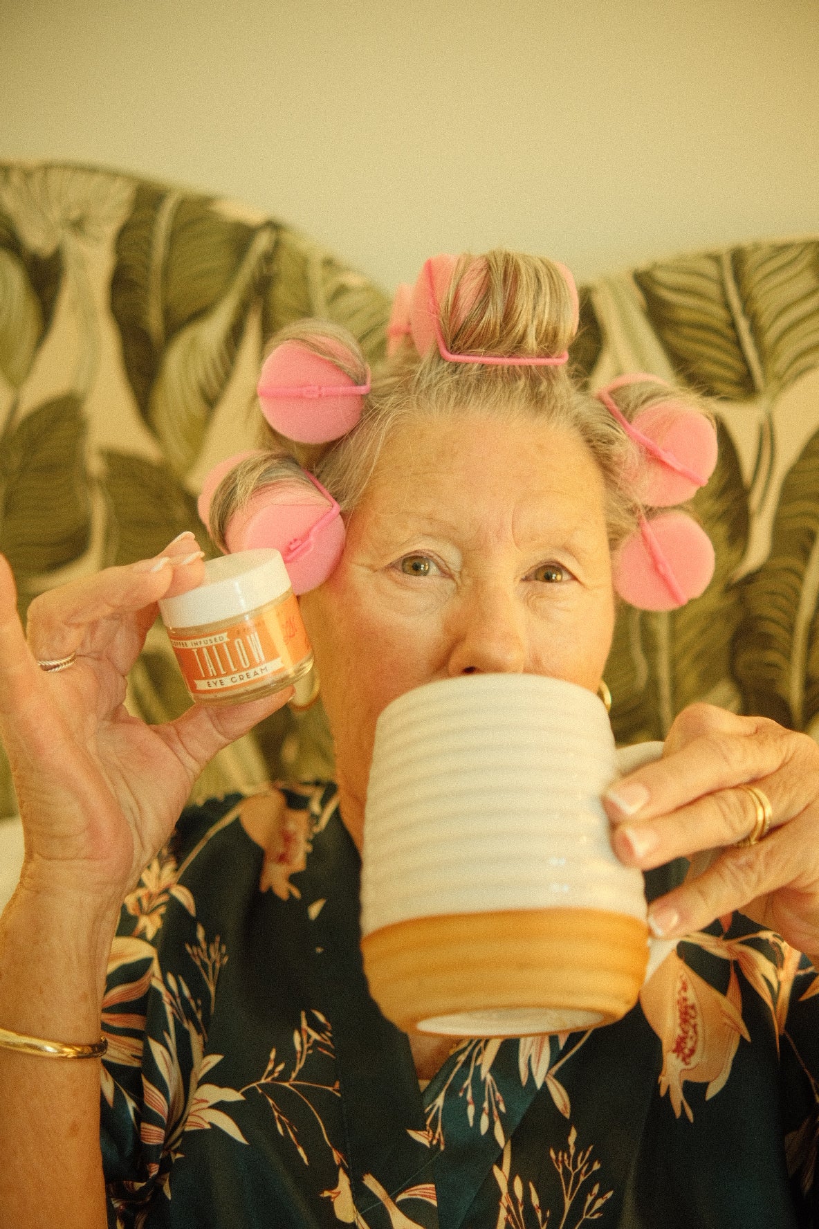 Person with pink hair rollers holding a container, wearing a floral dress.